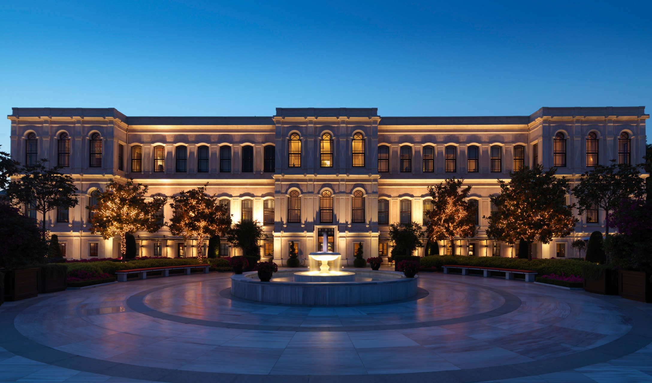 Illuminated grand luxury hotel facade with fountain courtyard at dusk