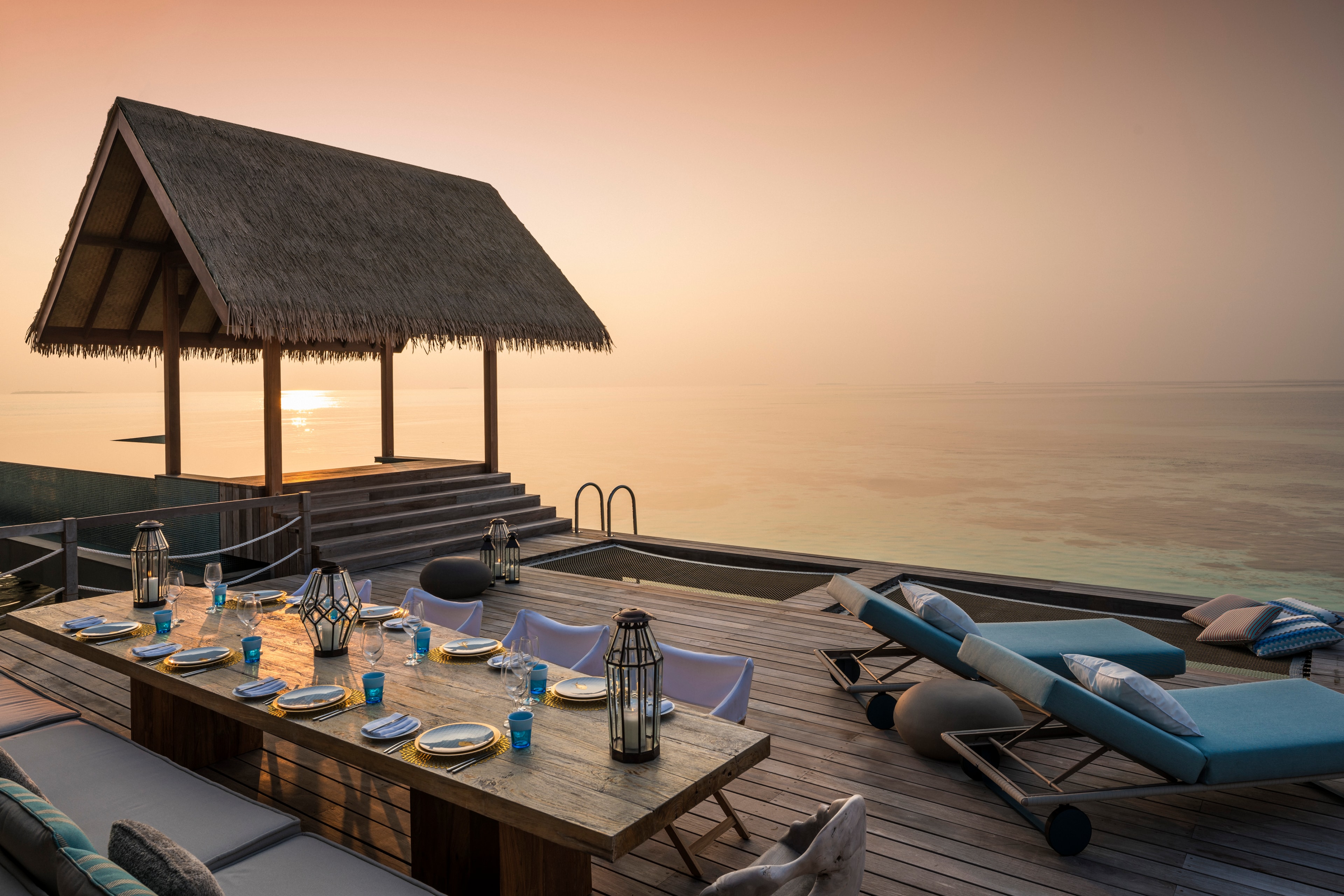 Overwater dining pavilion at sunset with elegant table setting and ocean views, Maldives